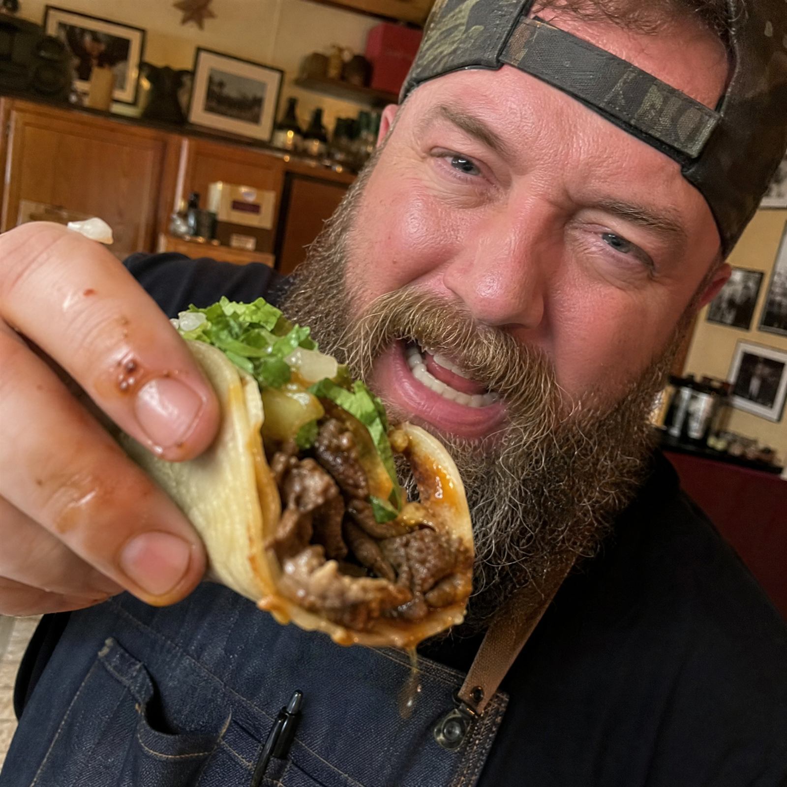 A person taking a big bite out of a loaded steak taco with lettuce and onion